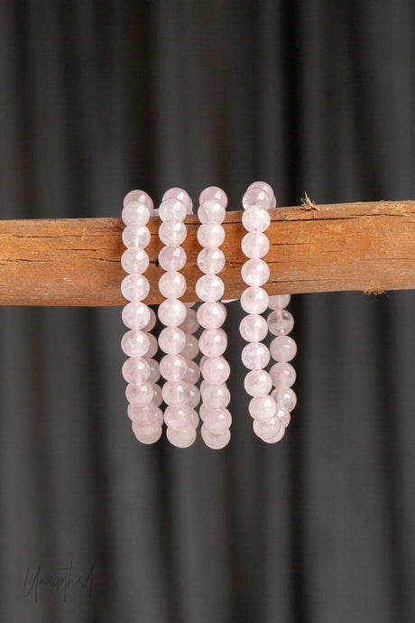 Four pink rose quartz beaded bracelets on a wooden stick against a dark background