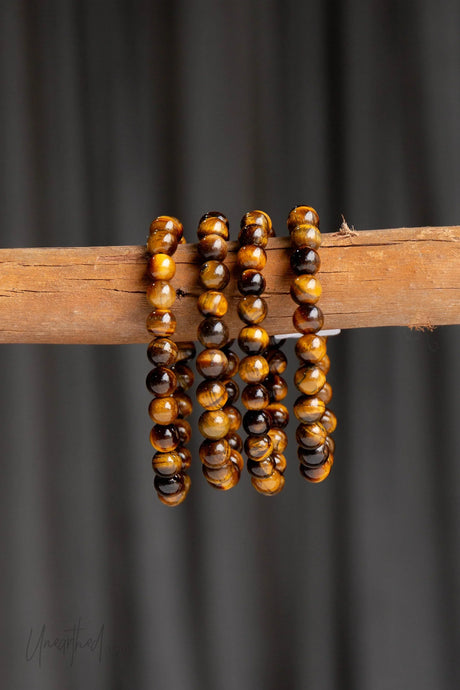 Stack of tiger eye bracelets on a wooden stick against a dark background