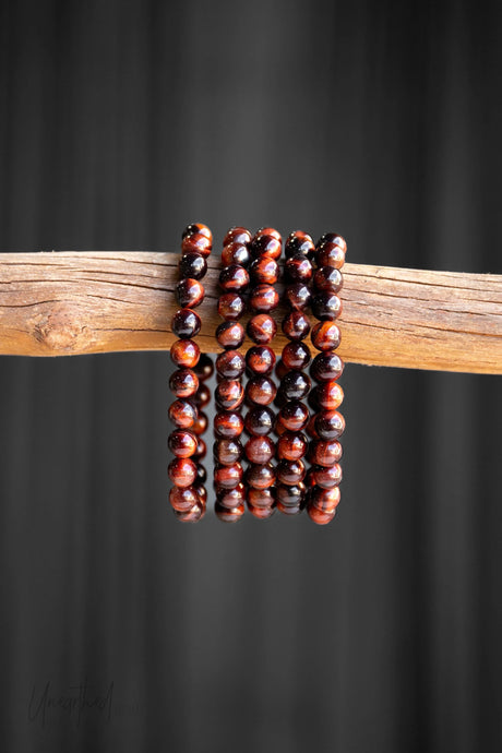 Red Tiger Eye beaded bracelets stacked on a wooden stick against a black background