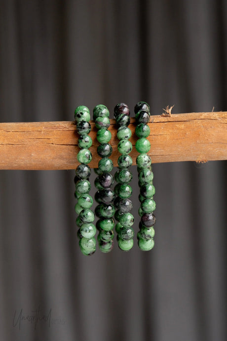 Green and black beaded bracelets on a wooden stick against a dark background