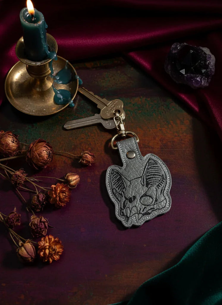 Keychain with bat skull design on a dark surface with candles and crystals