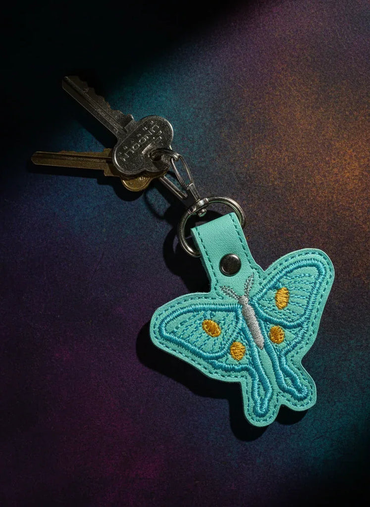Moth-shaped keychain attached to a key on a dark background