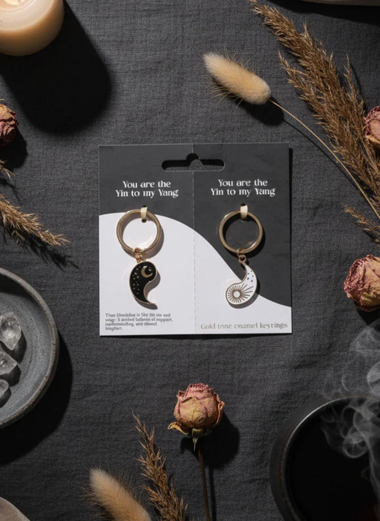 Pair of gold-tone keychains with black and white designs on a packaging card.