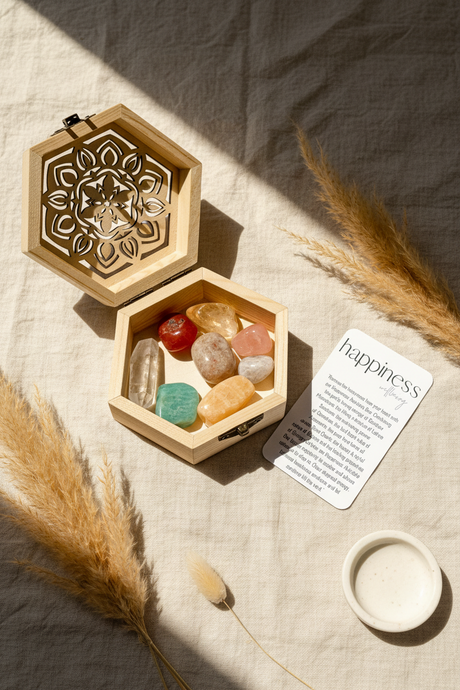 Hexagonal wooden box with colorful stones and a card labeled 'happiness' on a textured surface.