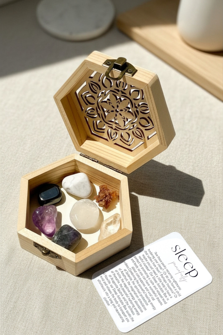 Hexagonal wooden box with decorative lid containing stones and a card on a light surface