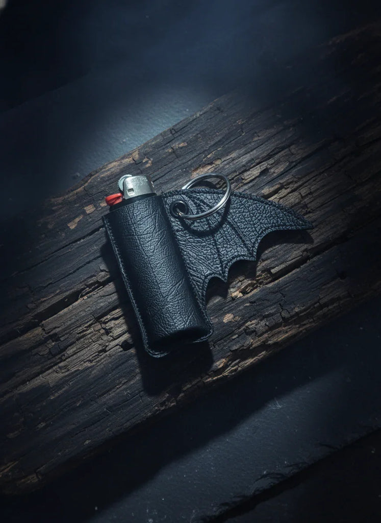 Black leather bat-shaped lighter case on a dark wooden surface