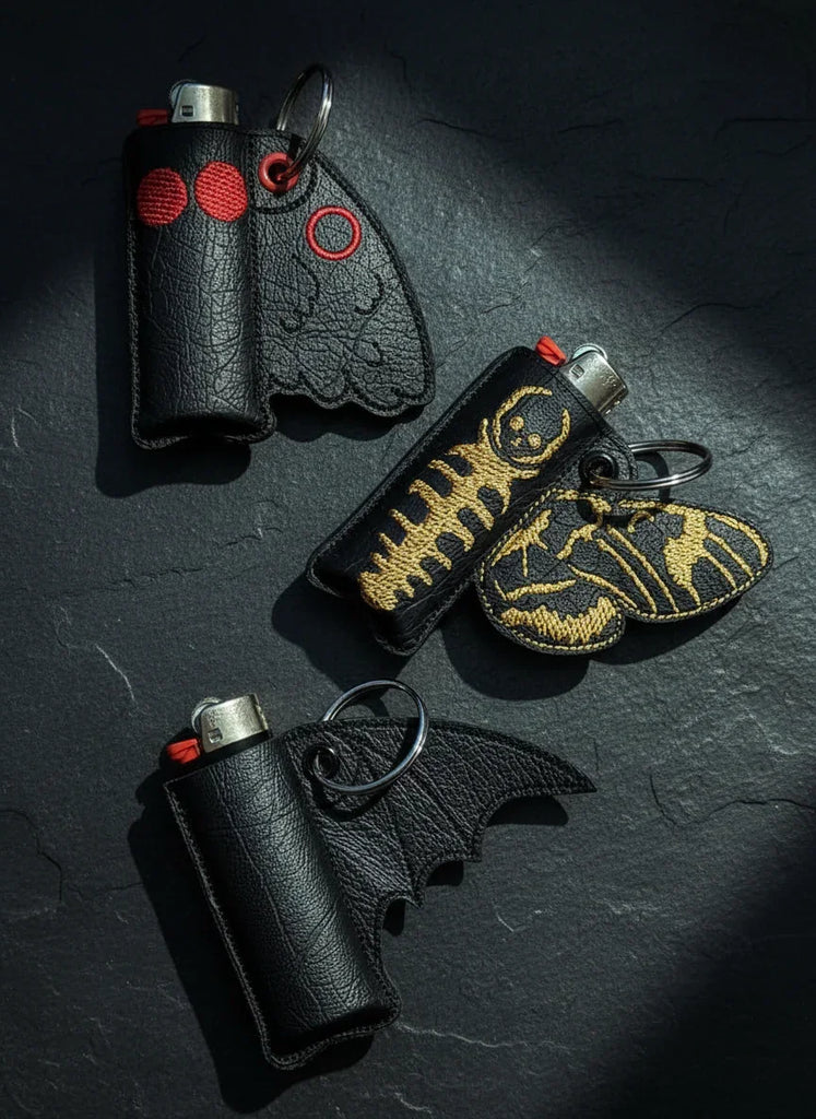 Three black leather lighters with batwing designs on a dark surface