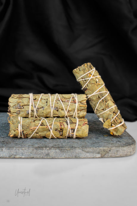 Three bundles of dried eucalyptus tied with white string, arranged on a gray stone slab against a black fabric backdrop.