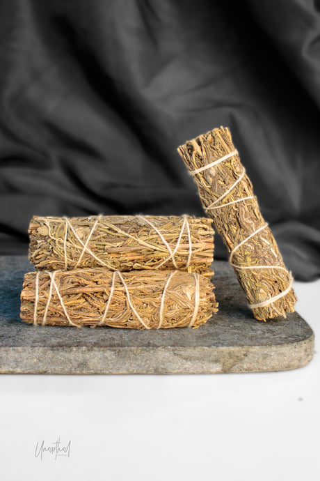 Three bundles of dried lavender tied with white string, arranged on a dark stone slab with a black fabric backdrop.