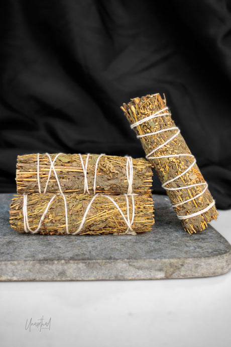 Three bundles of dried mugwort tied with white string, arranged on a gray stone slab against a black fabric background.
