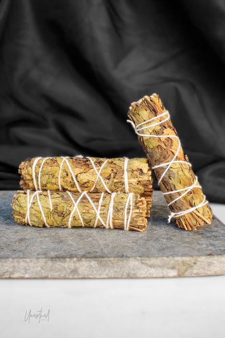 Three dried peppermint bundles wrapped in white string, arranged on a gray stone slab with a black fabric backdrop.