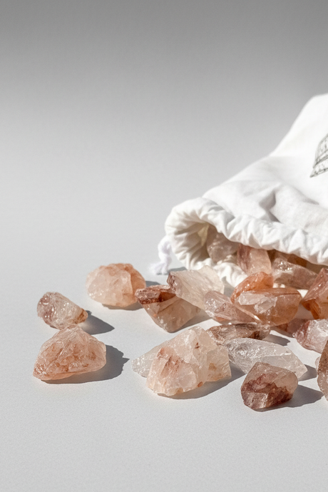 Fire Quartz crystal stones spilling out of a white drawstring bag on a light gray background