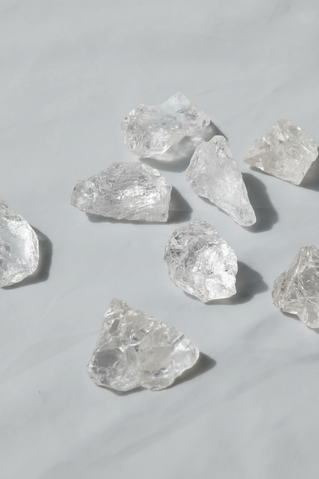Raw clear quartz scattered on a light gray background