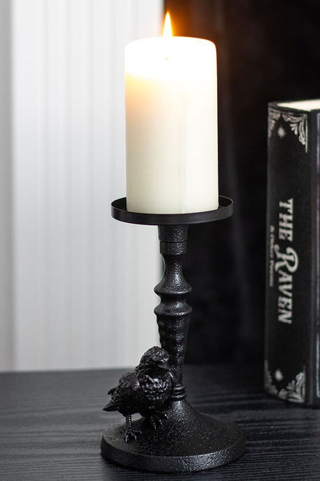 Decorative candle holder with a lit candle next to a book titled 'The Raven' on a wooden surface.