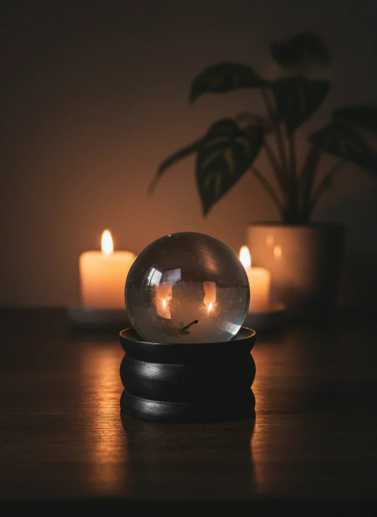 Quartz sphere with candles inside on a wooden surface, blurred plant in the background