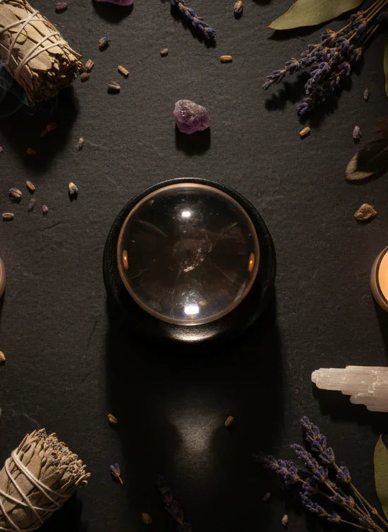 Crystal ball surrounded by crystals, herbs, and leaves on a dark surface