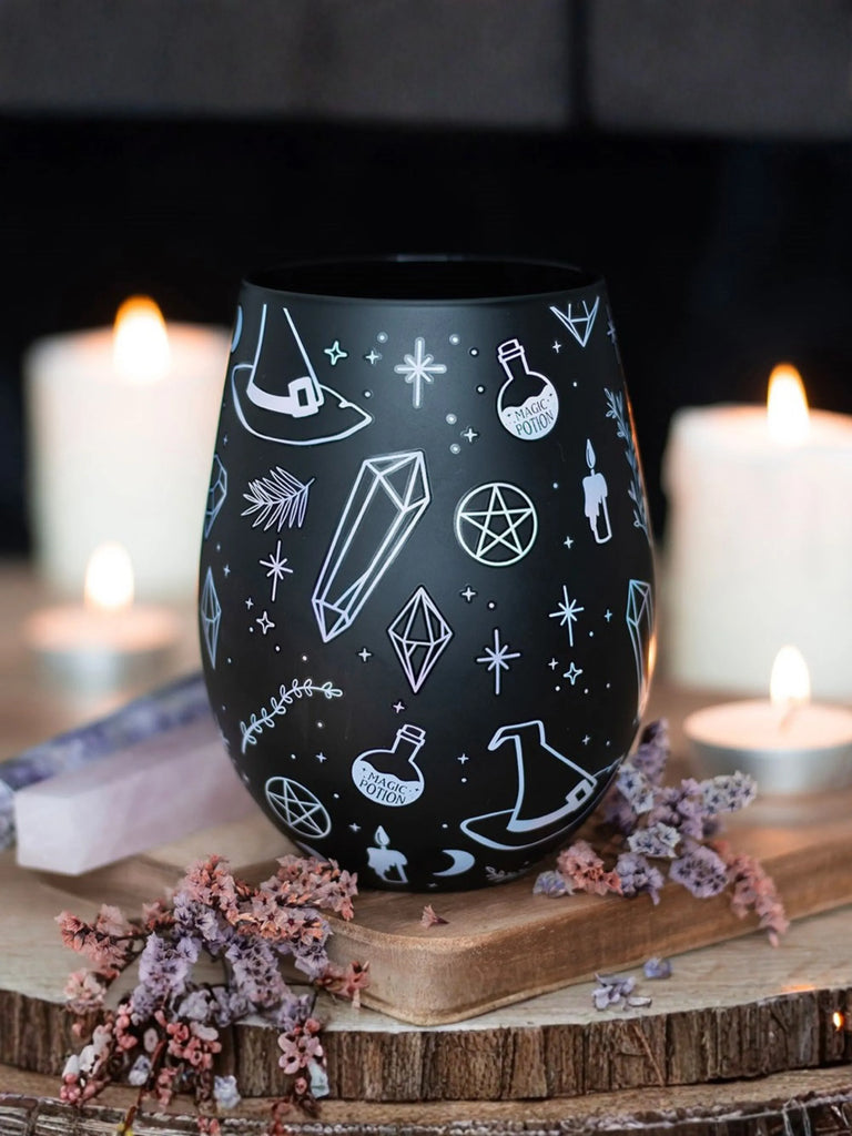 Black tumbler with white geometric designs on a wooden surface with candles in the background