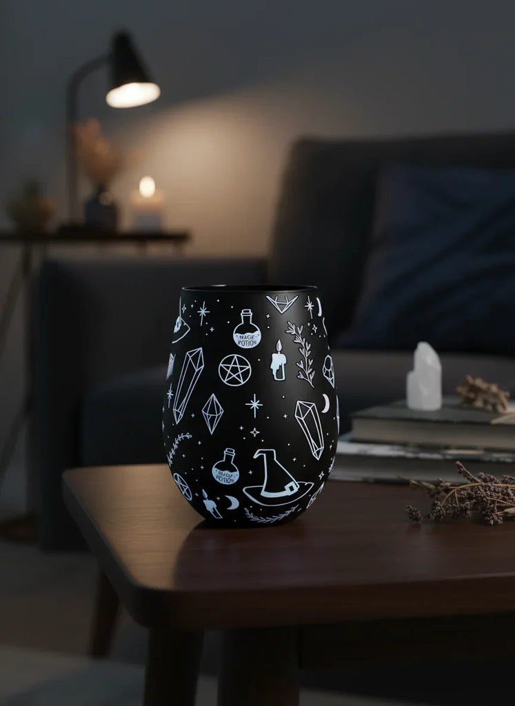 Black tumbler with white symbols on a wooden table in a dimly lit room.