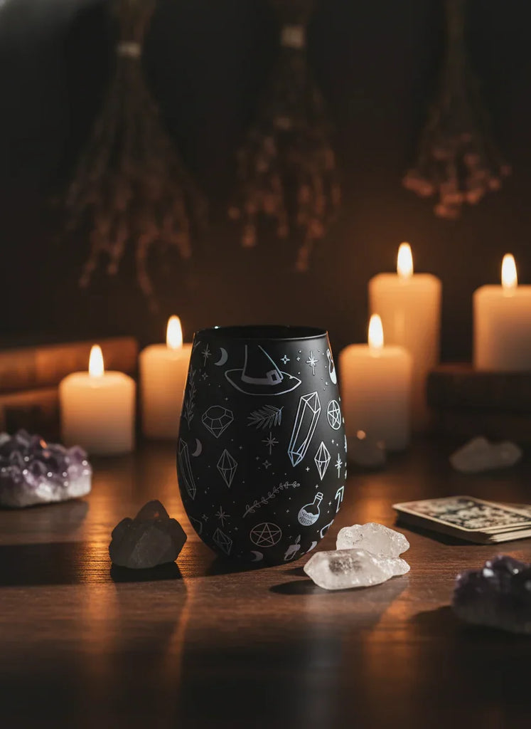 Black tumbler with mystical designs on a table with candles and crystals