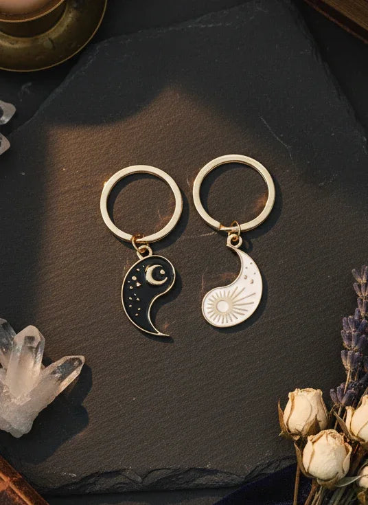 Yin yang keychains on a dark surface with flowers and crystals.