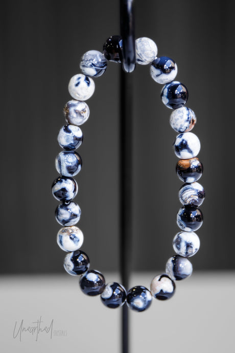 An Orca Agate bead stretch bracelet with a variety of beads displaying deep blue and black hues, and some with a white and grey color pattern, placed on a stretchy cord.