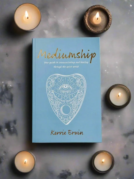 Book titled 'Mediumship' by Kerrie Erwin surrounded by lit candles on a textured surface.