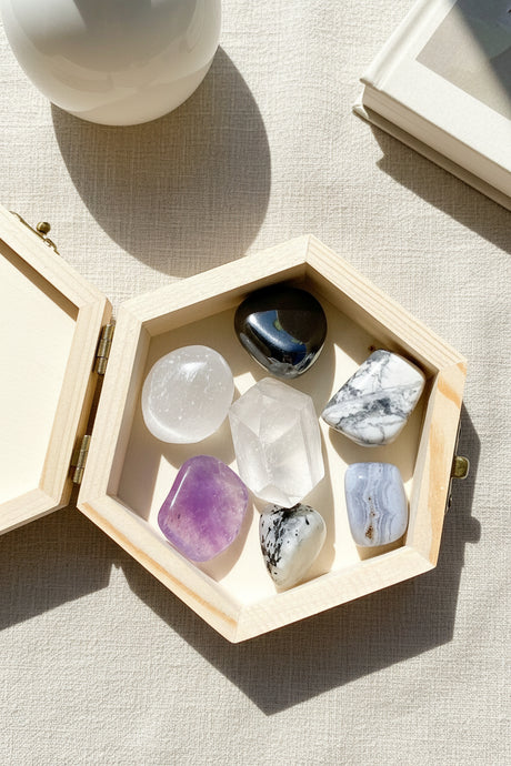 Hexagonal wooden box with various crystals to assist with Migraines on a textured surface