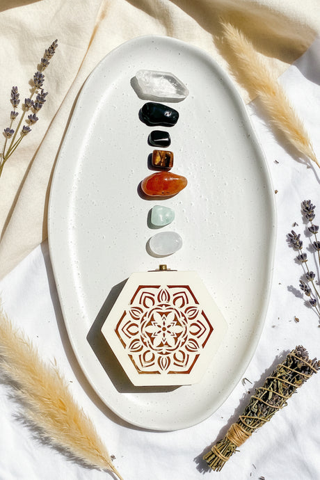 White oval dish with PROTECTION crystals and a decorative BOX on a white fabric background with lavender and feathers.