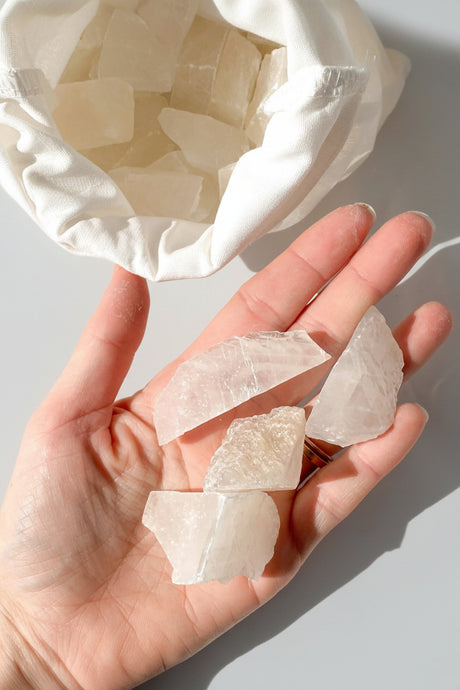 Hand holding white calcite stones with a white fabric bag in the background
