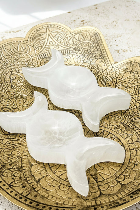 Two white selenite triple moon trinket bowls on a decorative brass plate